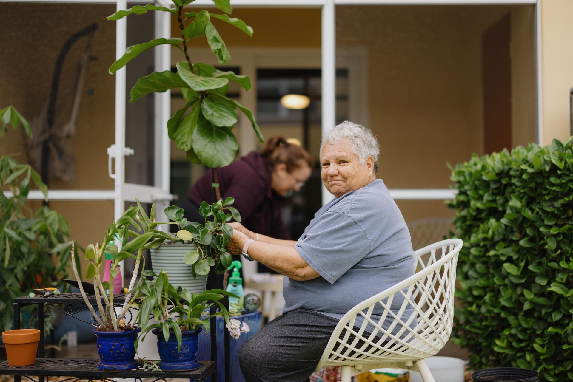 Senior woman gardening on patio with another woman helping in background
